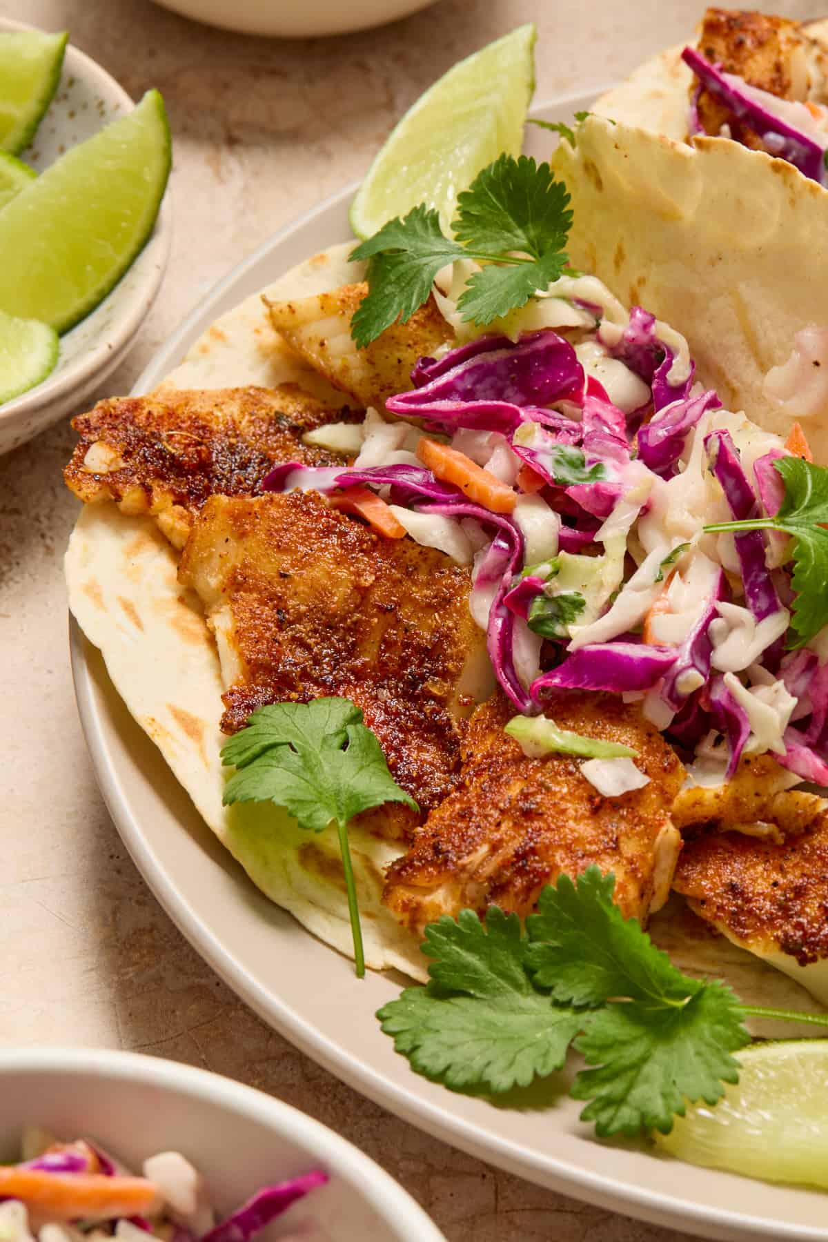 Air fryer fish tacos on white plate with slaw and fresh cilantro.