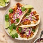 Air fryer fish tacos on white plate with lime and cilantro over top.