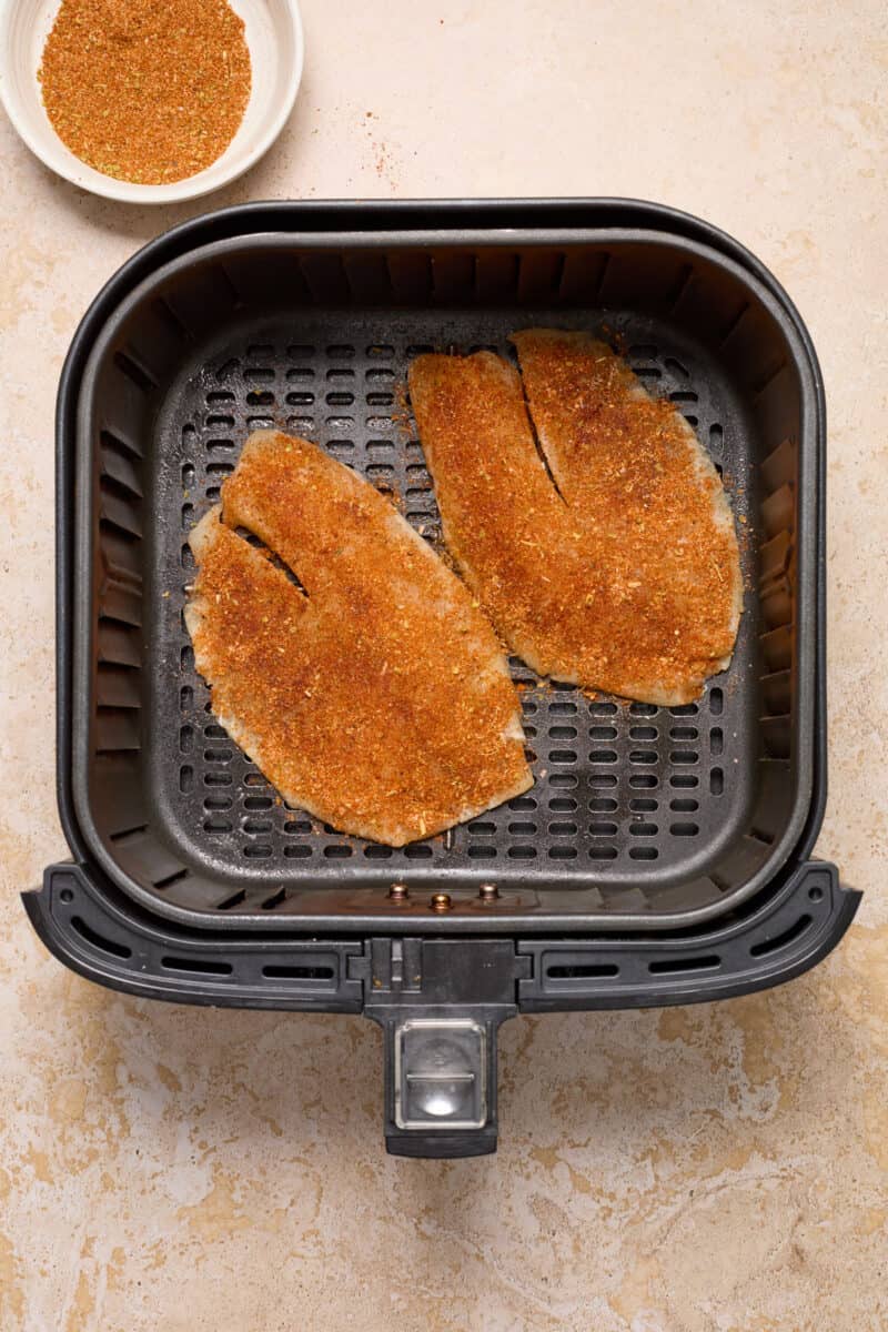 Fish tacos in air fryer with seasoning covering the fish.