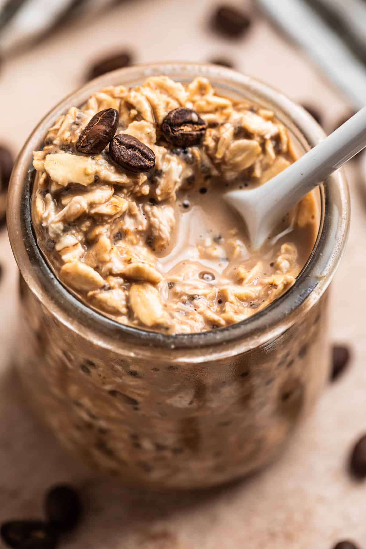 Coffee overnight oats with white spoon scooping into jar and coffee beans on top.