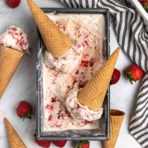 Overhead view of strawberry ice cream in container with cones and fresh strawberries.