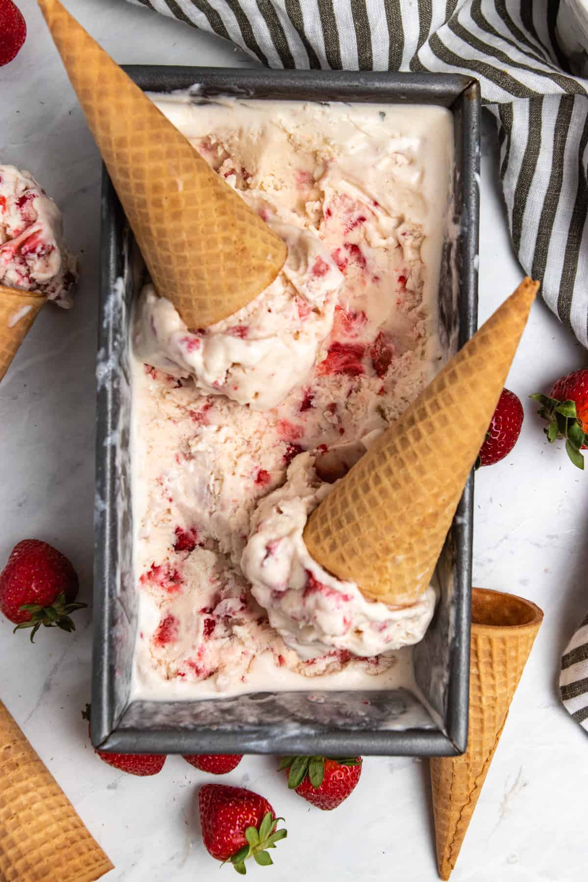 Strawberry ice cream in bread pan loaf with scoops and sugar cones.