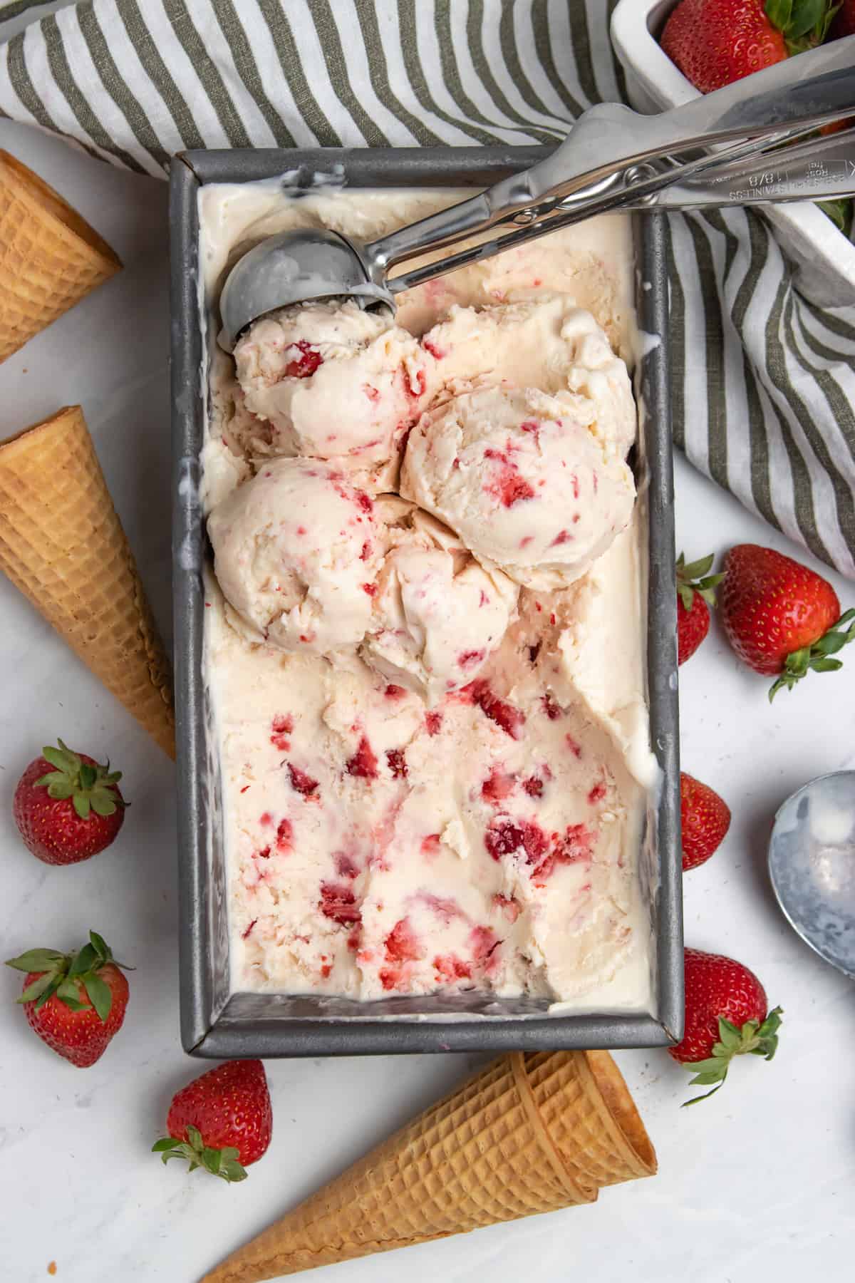 Strawberry ice cream in bread pan with ice cream scoop.