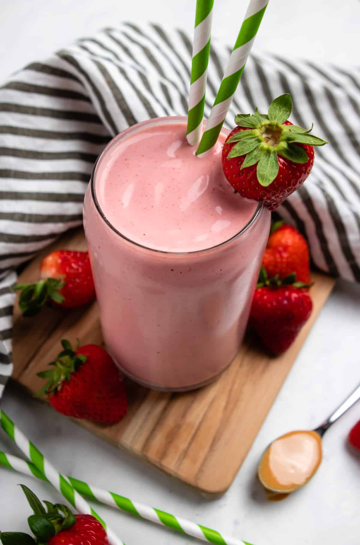 Strawberry Peanut butter smoothie in glass with green straws and strawberry garnish.