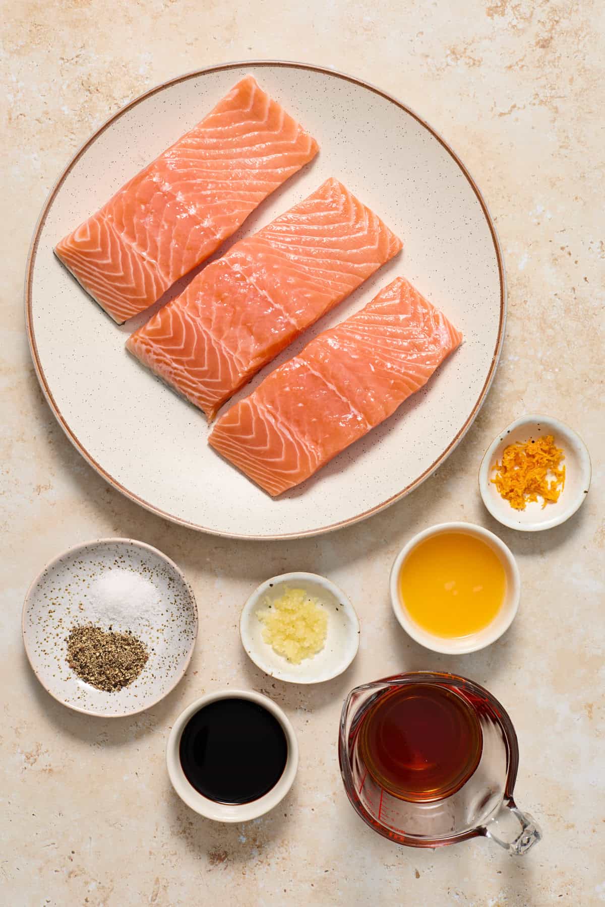 Salmon, orange zest, maple syrup and other ingredients arranged on surface to make glazed salmon.