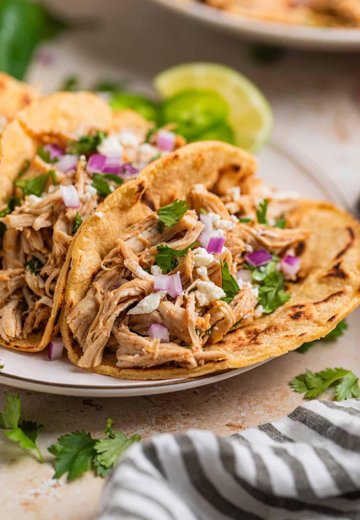 Instant pot shredded chicken tacos in charred corn tortillas topped with onion, cheese and cilantro.