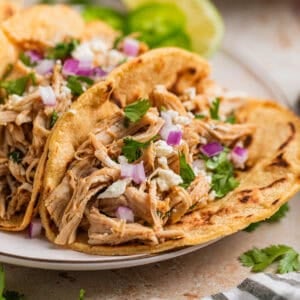 Instant Pot shredded chicken tacos on plate with queso fresco, red onion and cilantro on top.