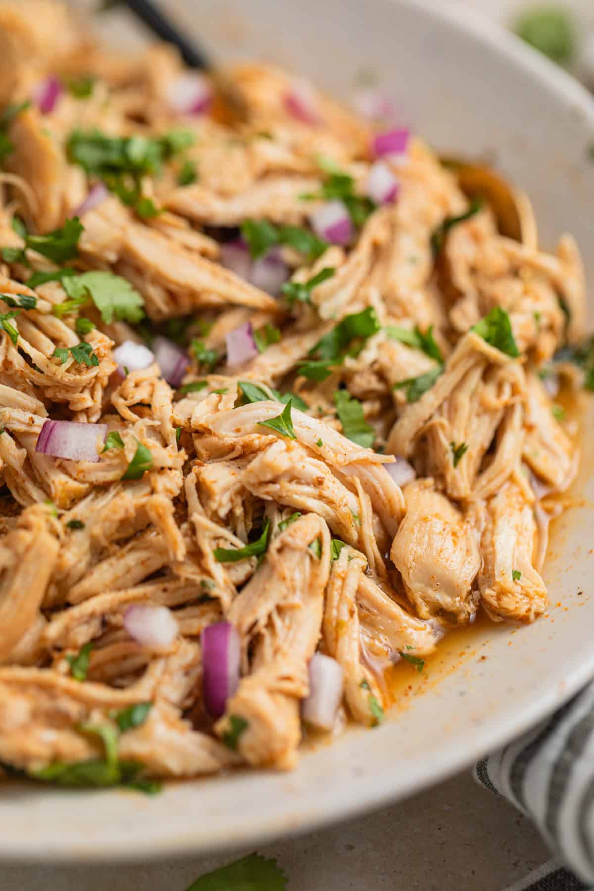 Shredded instant pot chicken in bowl with cilantro and red onion on top.
