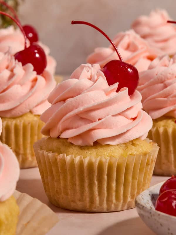 Pineapple cupcakes on surface with cherry frosting and cherry on top.