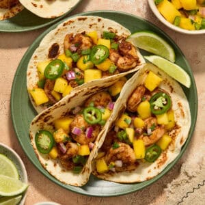 Three shrimp tacos on green plate topped with a salsa made of diced mango, onion and jalapeños.