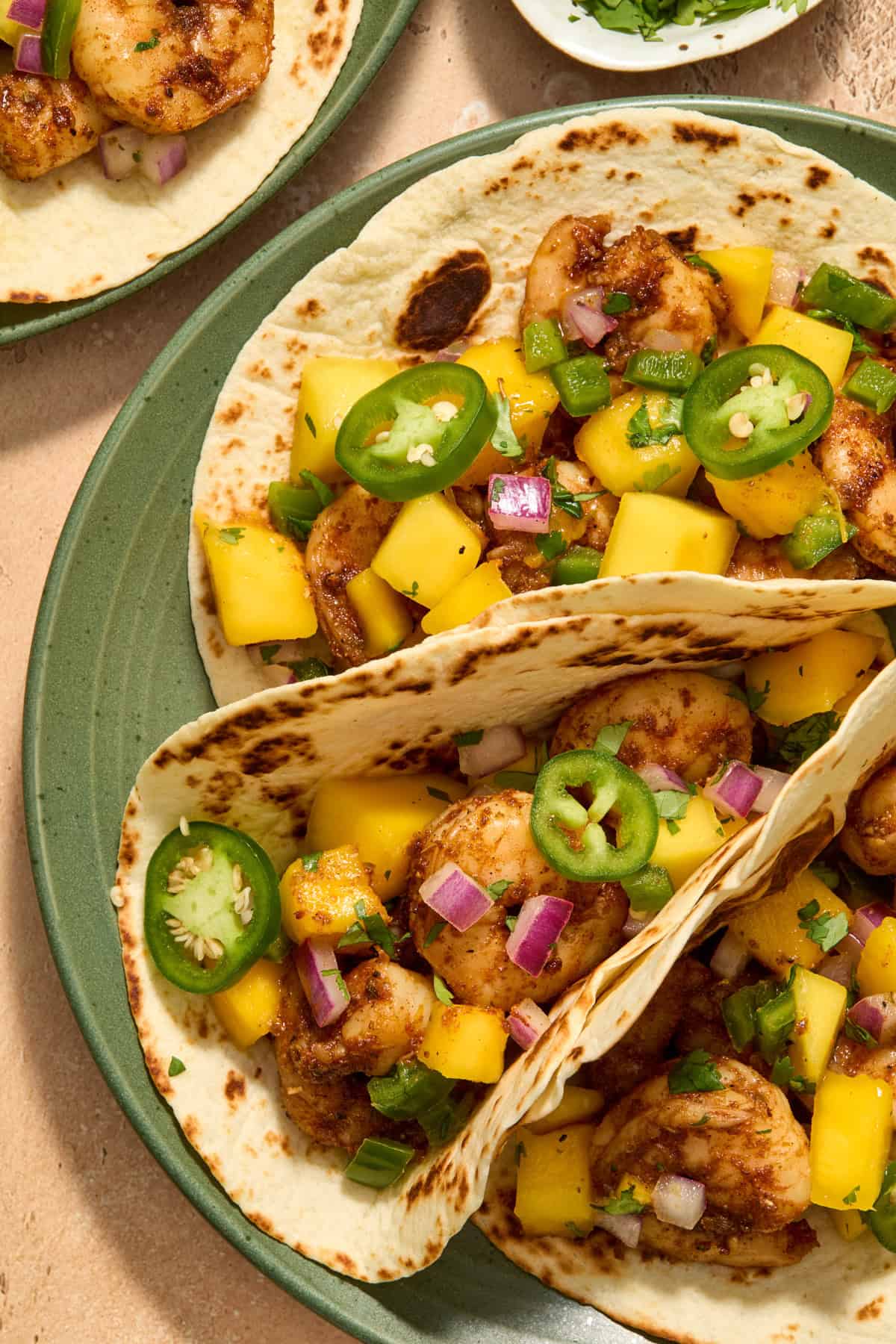 View of tortillas with spicy shrimp and mango salsa on top on green plate.