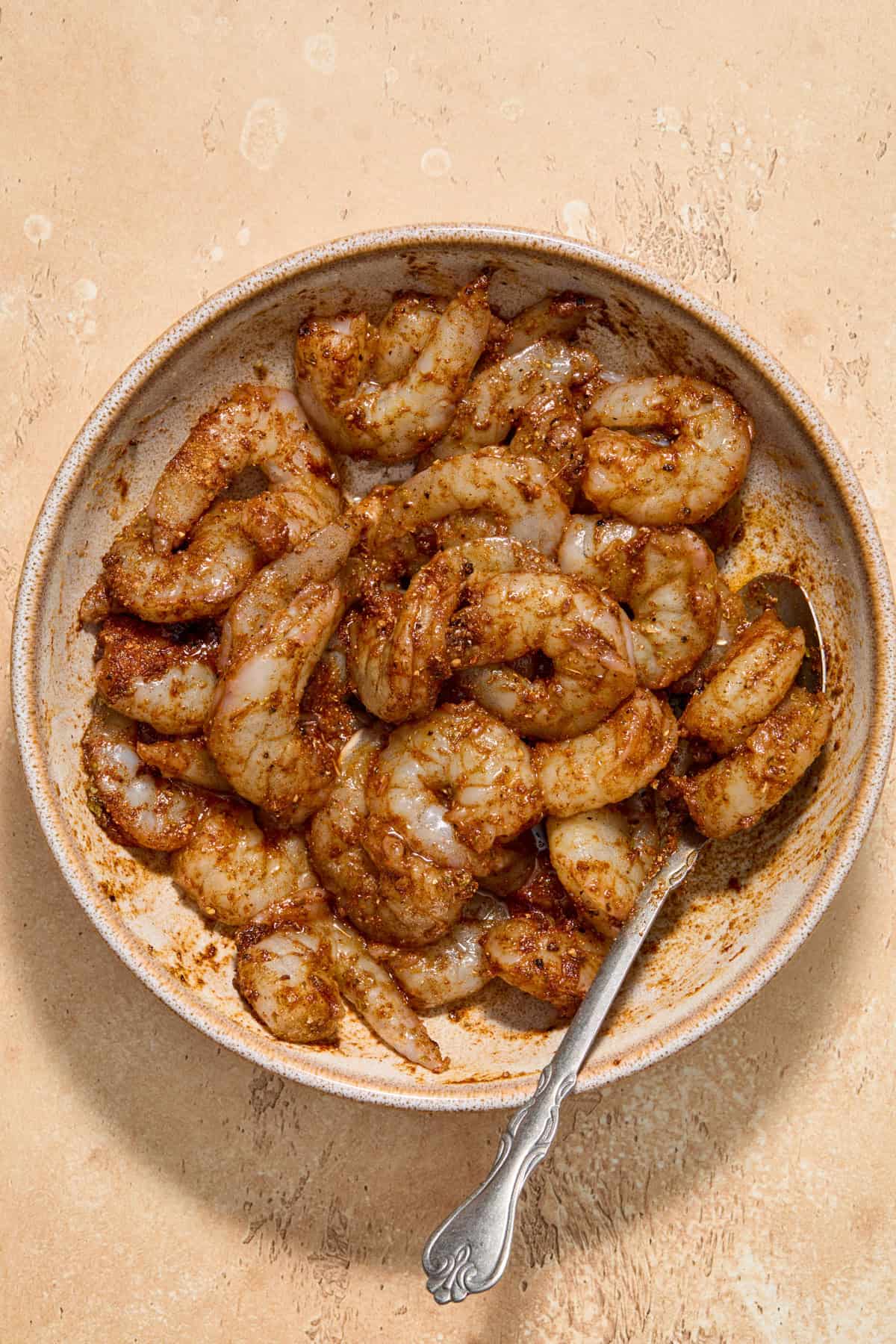 Seasoned shrimp in bowl with spoon before cooking.