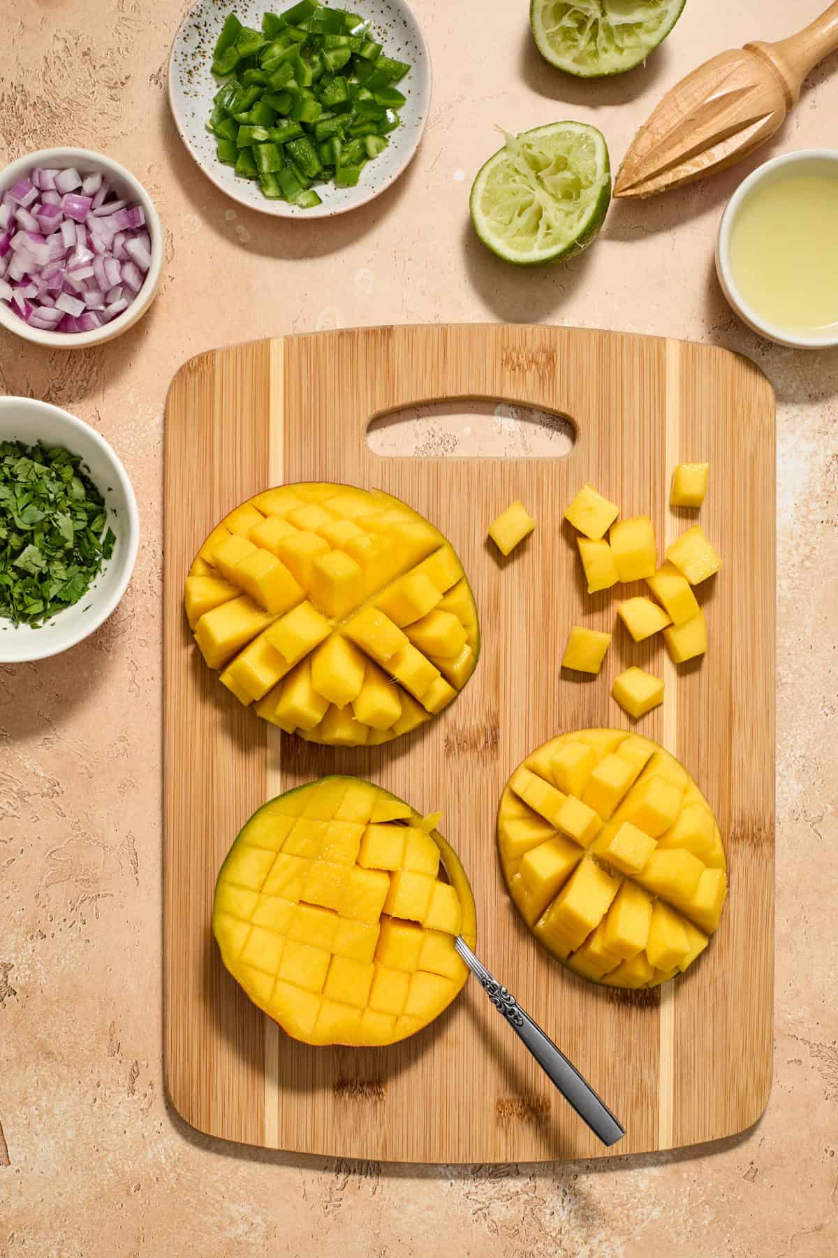 Diced mangos on cutting board with juiced lime, onion and other ingredients around it.