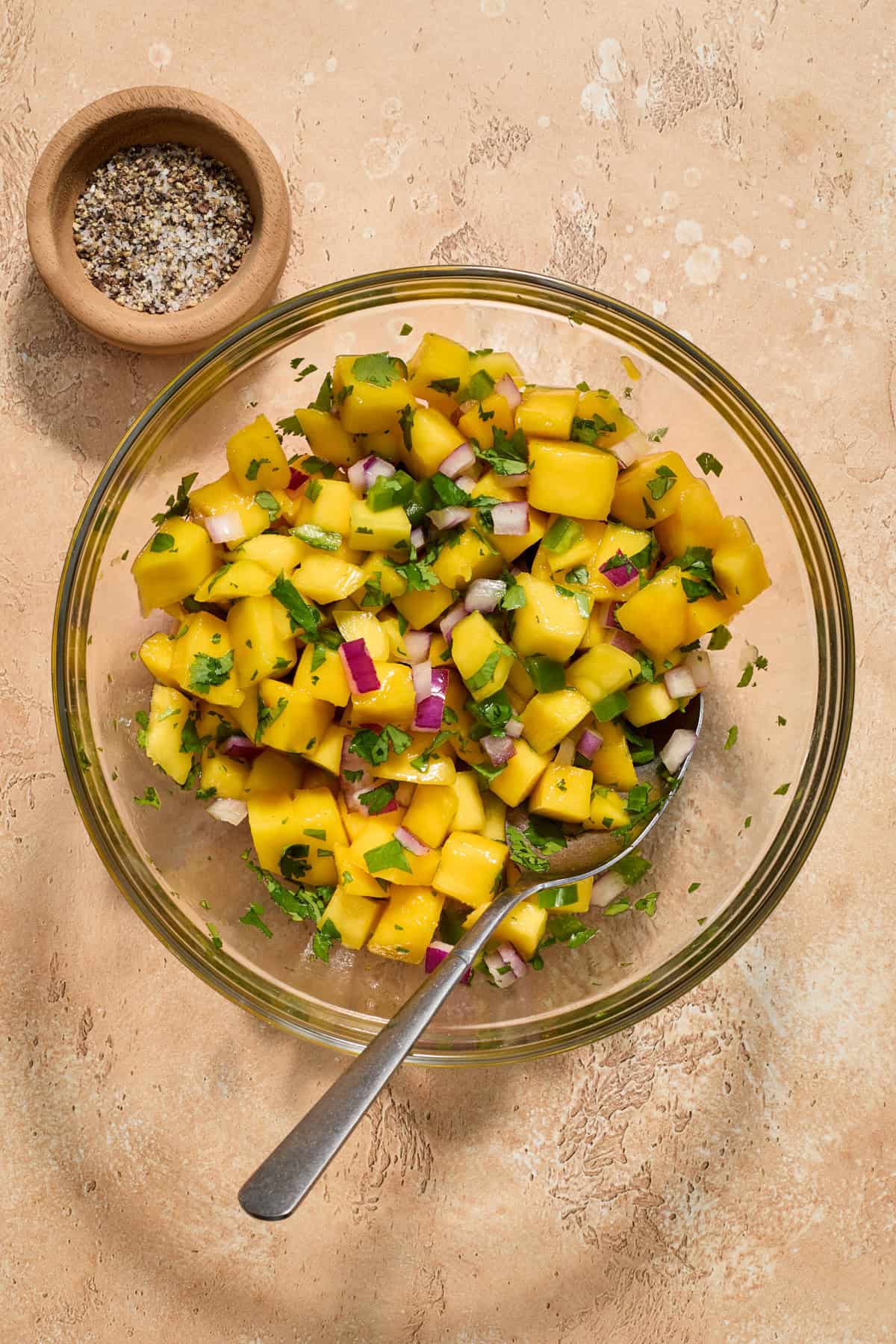 Mango salsa in bowl with salt and pepper beside it.