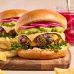Black bean burger on wood board topped with pepper jack cheese, guacamole, and pickled onions.