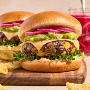 Black bean burger on wood board topped with pepper jack cheese, guacamole, and pickled onions.