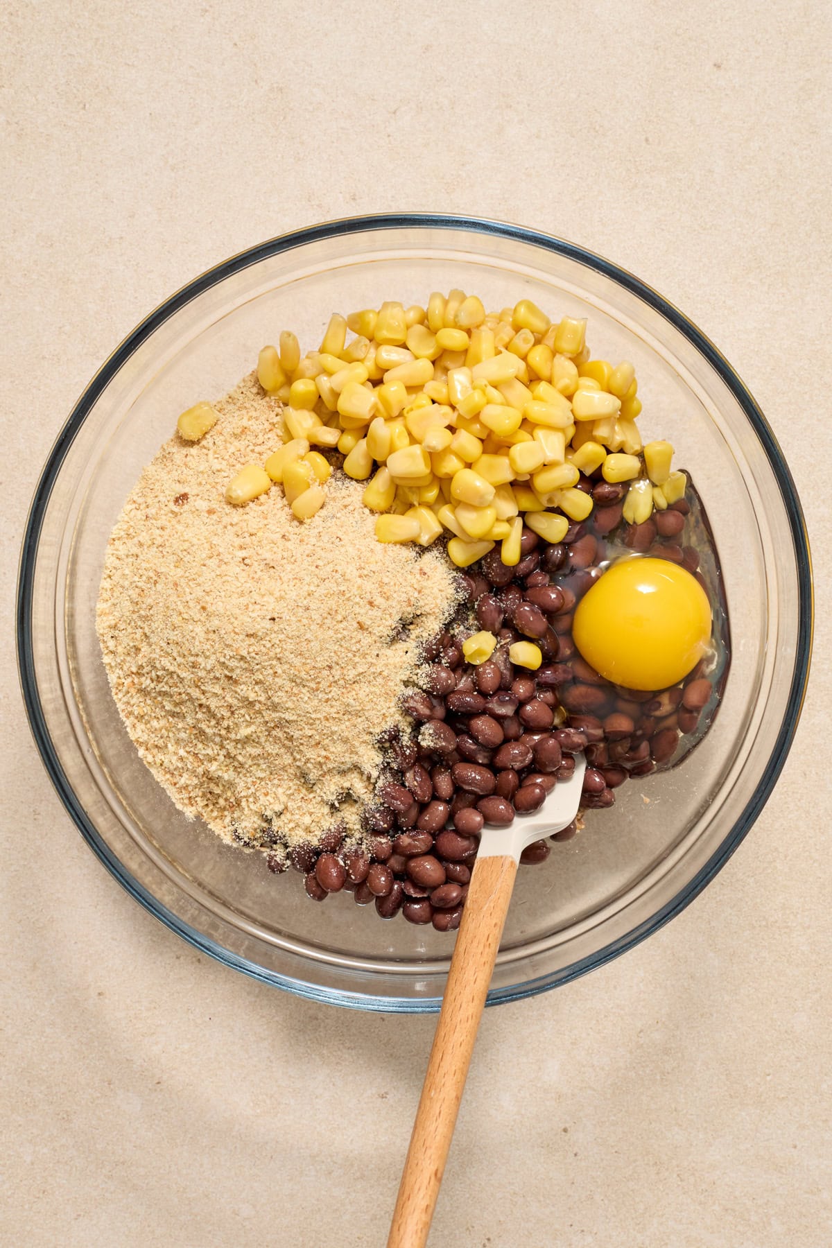 Breadcrumbs, black beans, eggs and corn added to mixing bowl with spatula.