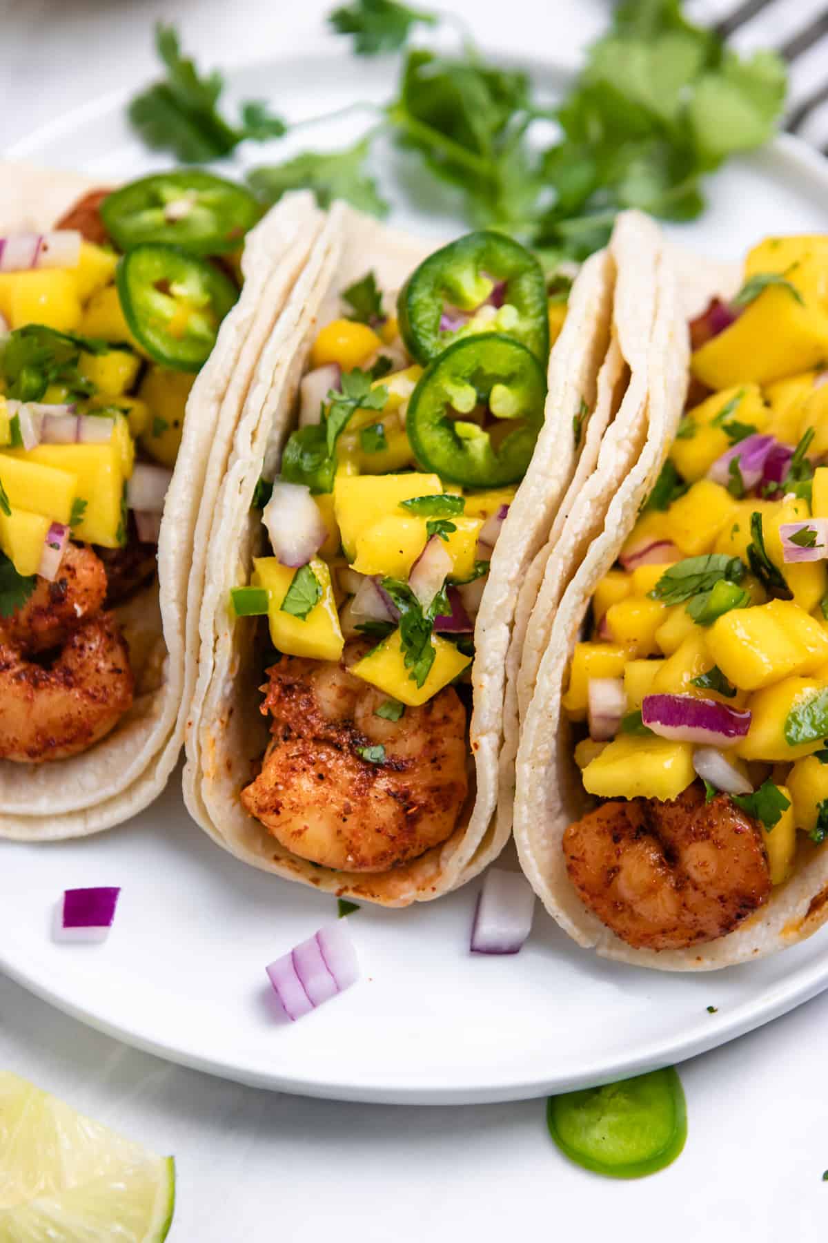 3 spicy shrimp tacos in corn tortillas covered with mango salsa on white plate.