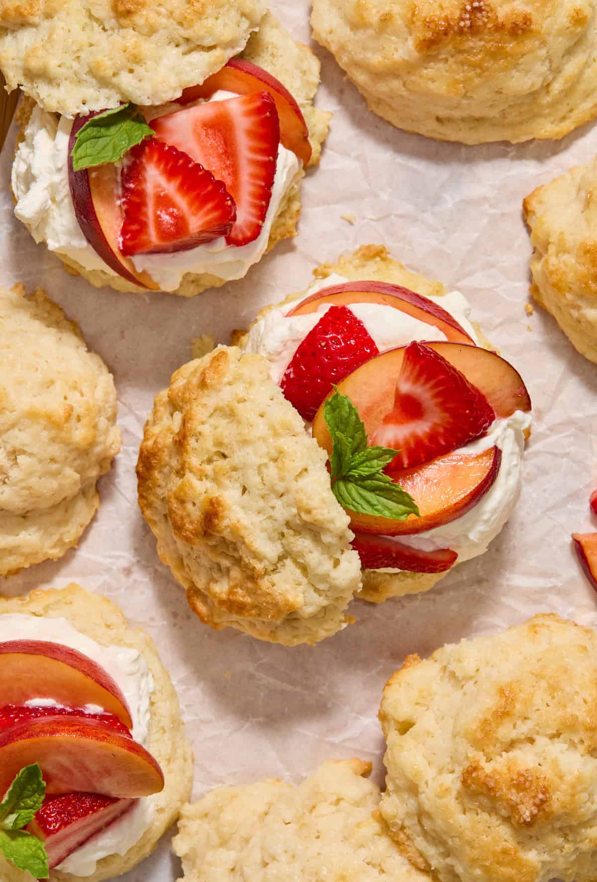 Overhead view of strawberry peach shortcakes with buttermilk biscuit tops propped to the side to show fruit and mint leaves on whipped cream.