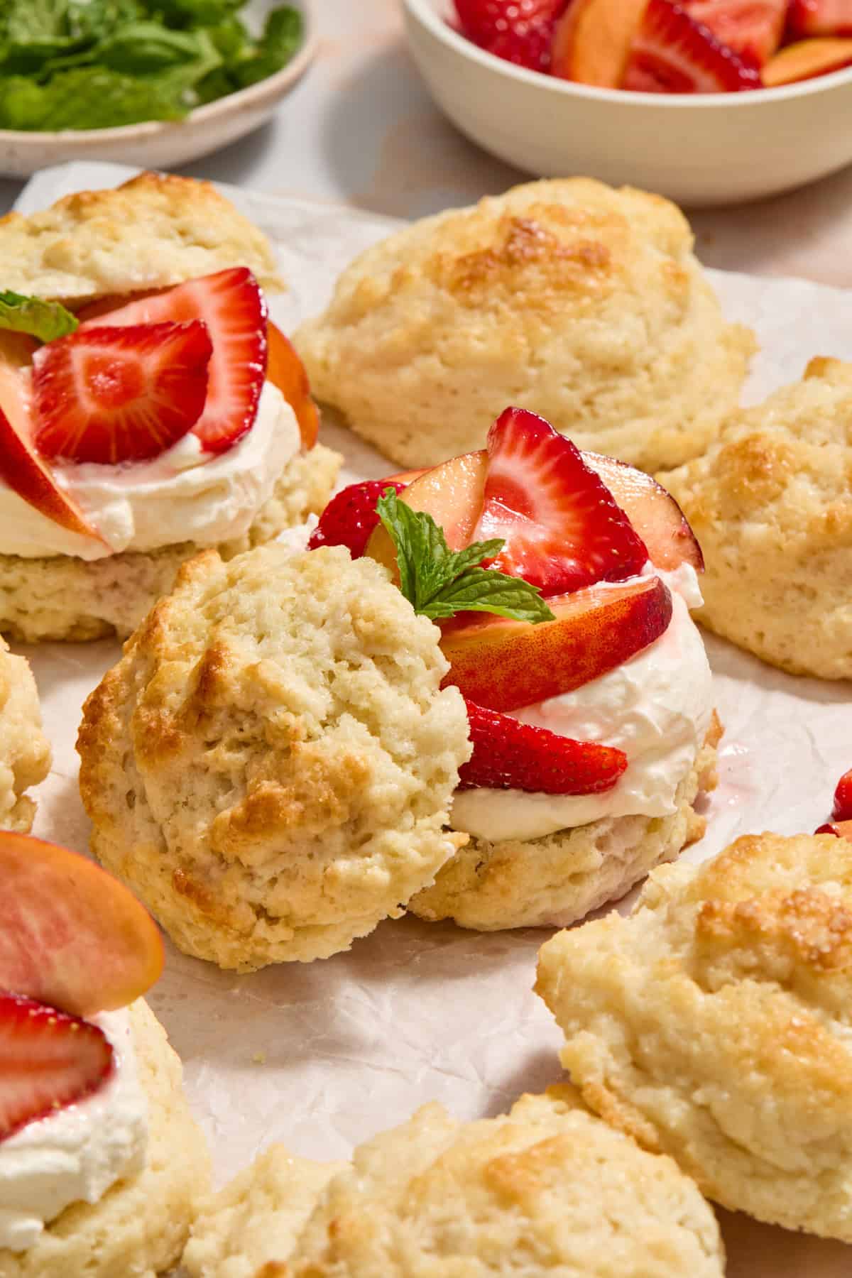 Peach and strawberry shortcakes layered with whipped cream and biscuit tops propped to the side of bottom half.