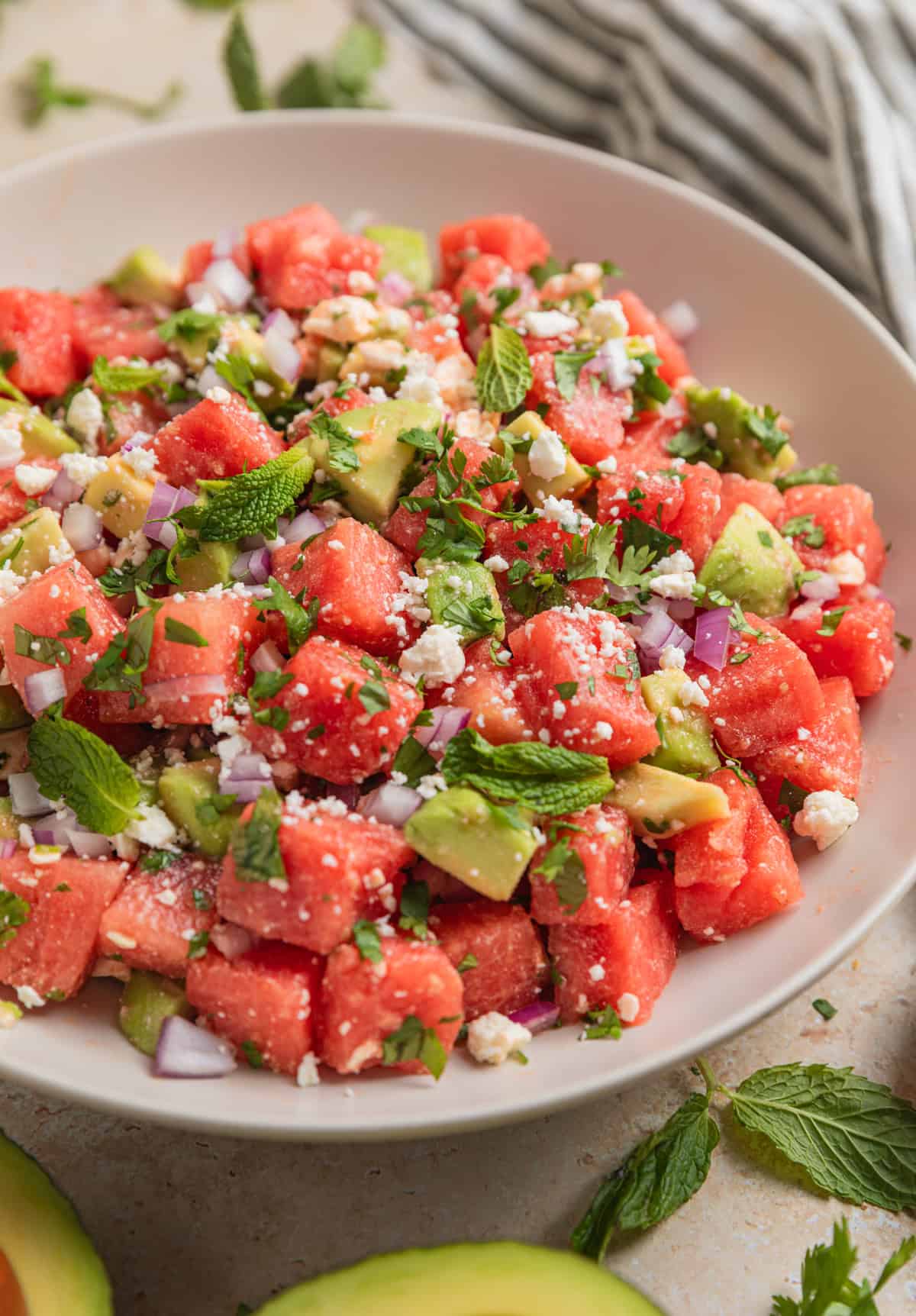 Watermelon salad with cubed avocado and feta in bowl topped with chopped cilantro and mint leaves.