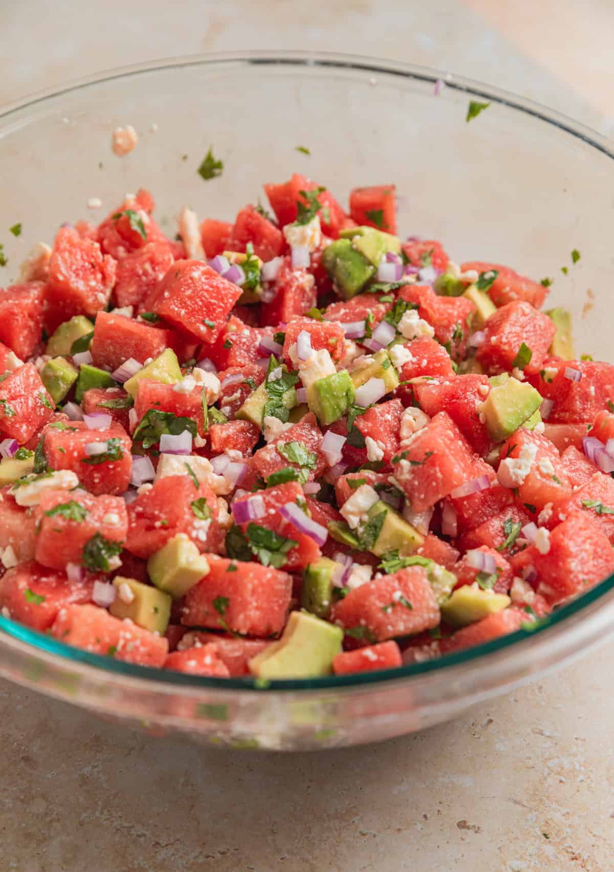 Watermelon avocado salad tossed in large glass bowl.
