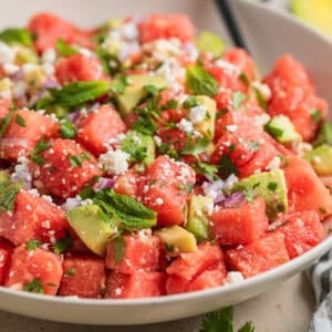 Bowl with watermelon salad with feta and avocado and spoon scooping into it.