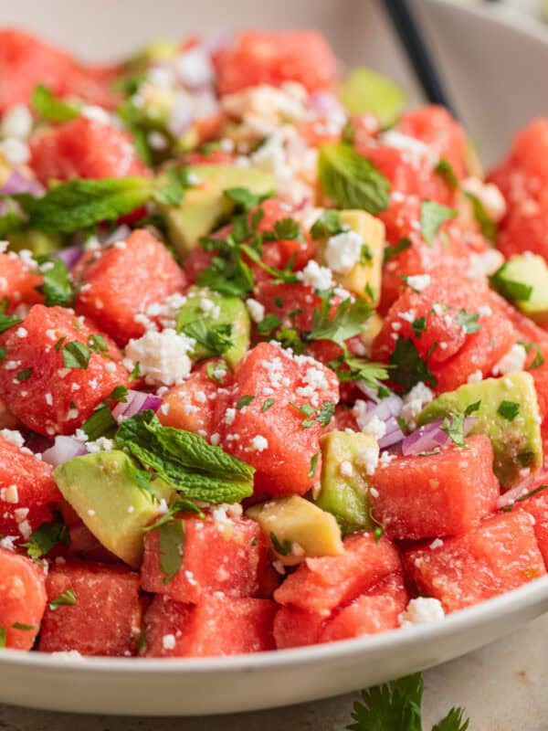 Bowl with watermelon salad with feta and avocado and spoon scooping into it.