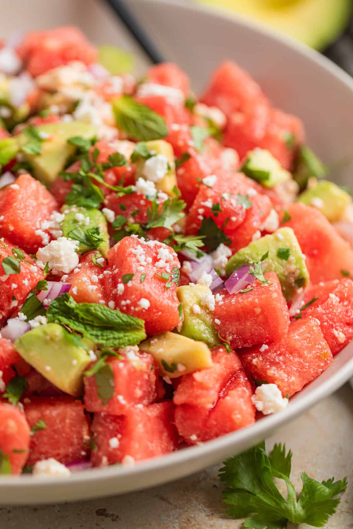 Watermelon avocado salad with feta and cilantro on top in bowl with spoon.