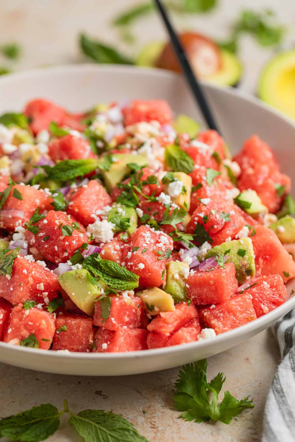 Salad bowl with watermelon, feta and avocado salad with spoon.