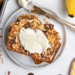 Coconut chip banana bread on white plate with butter spread on top.