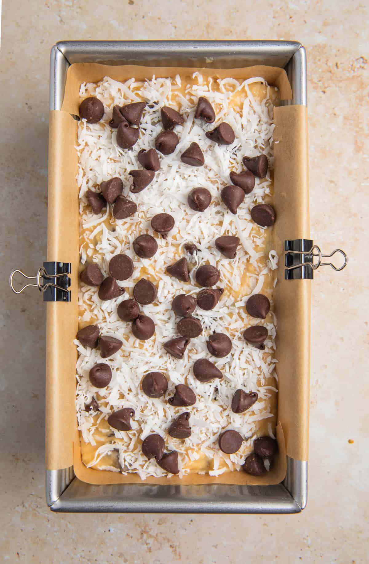 Pan with coconut banana bread batter topped with chocolate chips and coconut.
