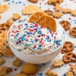 White bowl with funfetti cake dip with two waffle cookies dipping into it.