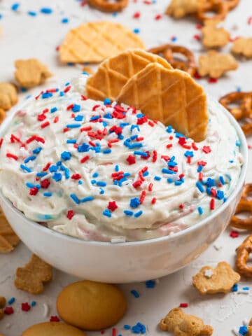 White bowl with funfetti cake dip with two waffle cookies dipping into it.
