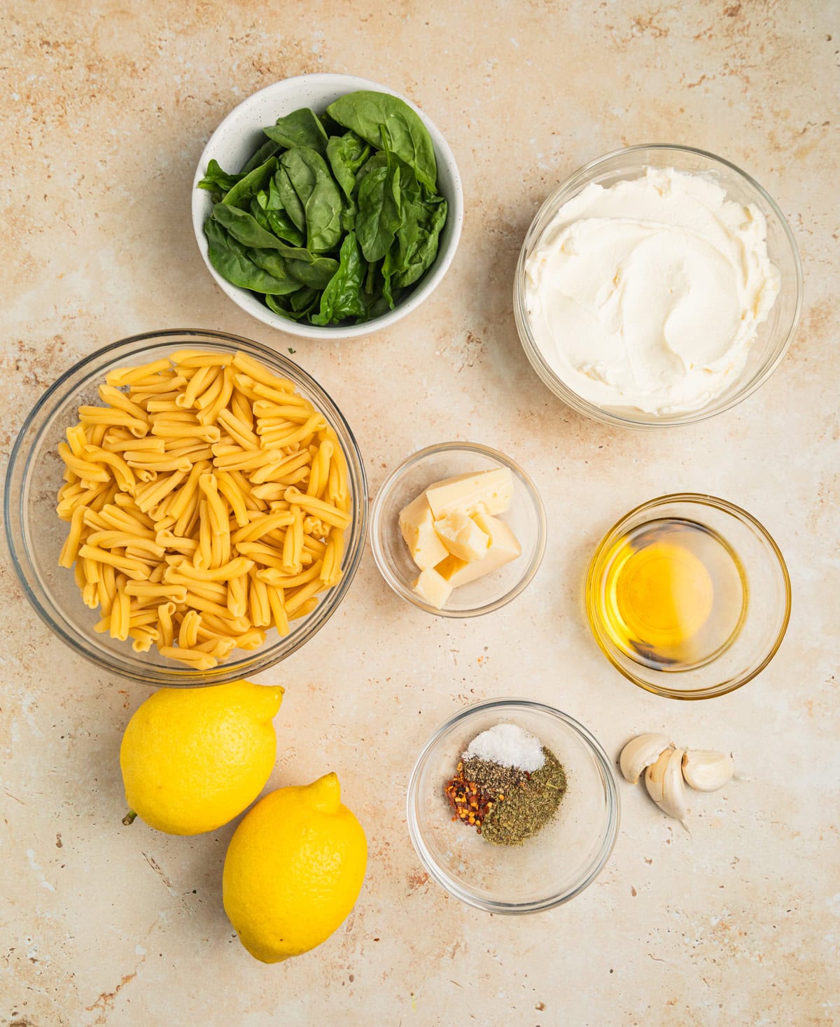 Pasta, lemons, spinach, olive oil and other ingredients on surface.