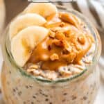 Glass jar with protein overnight oatmeal topped with sliced bananas and peanut butter.