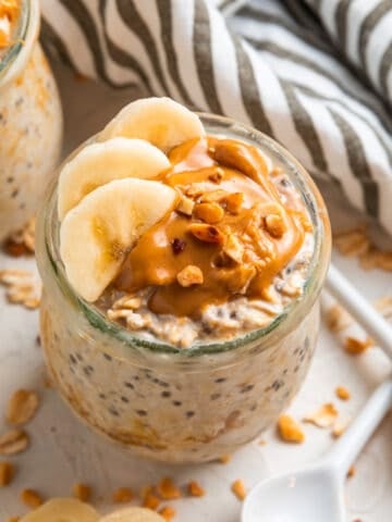 Glass jar with overnight oats topped with sliced banana and topped with peanut butter.