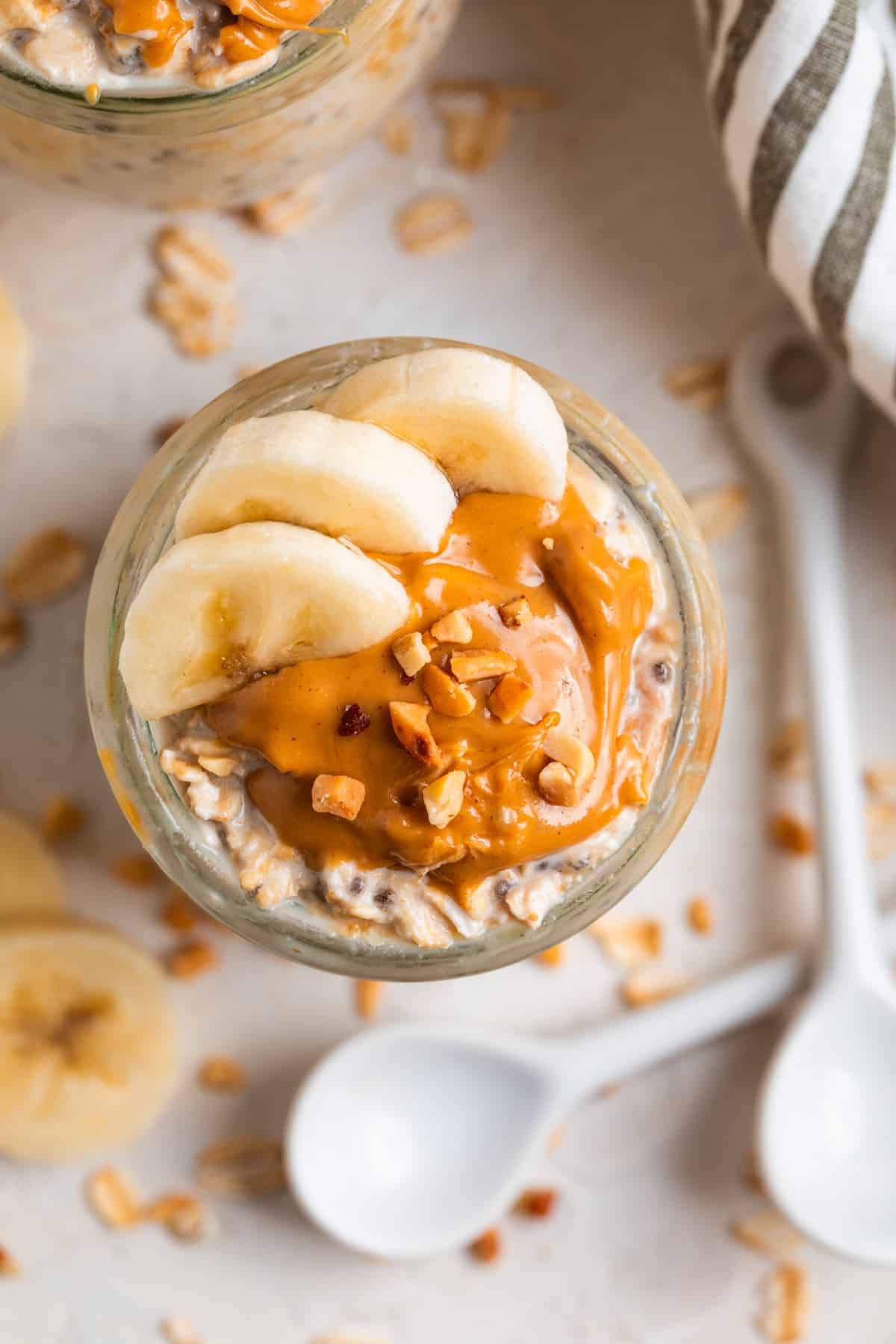 Overhead view of oatmeal topped with sliced bananas and peanut butter with white spoon and rolled oats surrounding.
