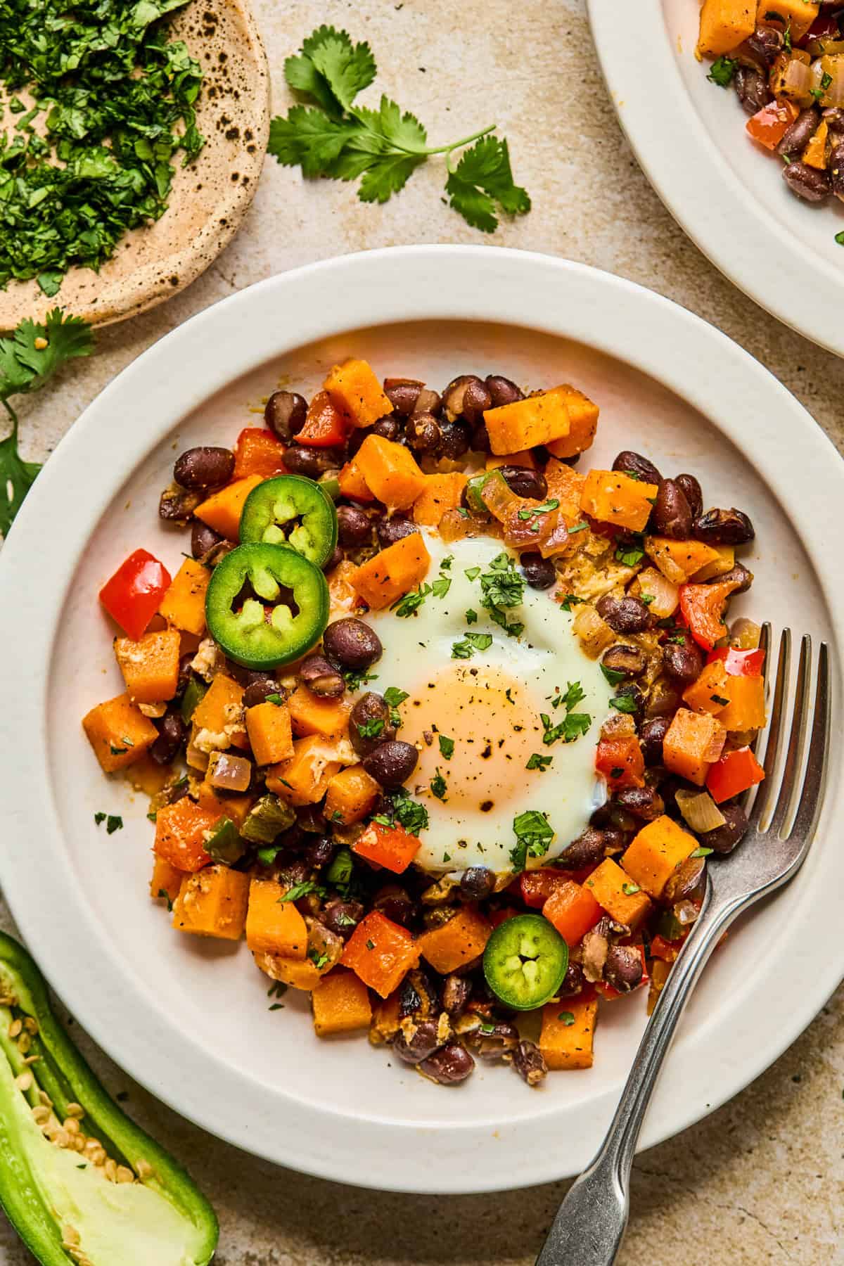 Plate with sweet potato breakfast hash and egg topped with jalapeño and cilantro.