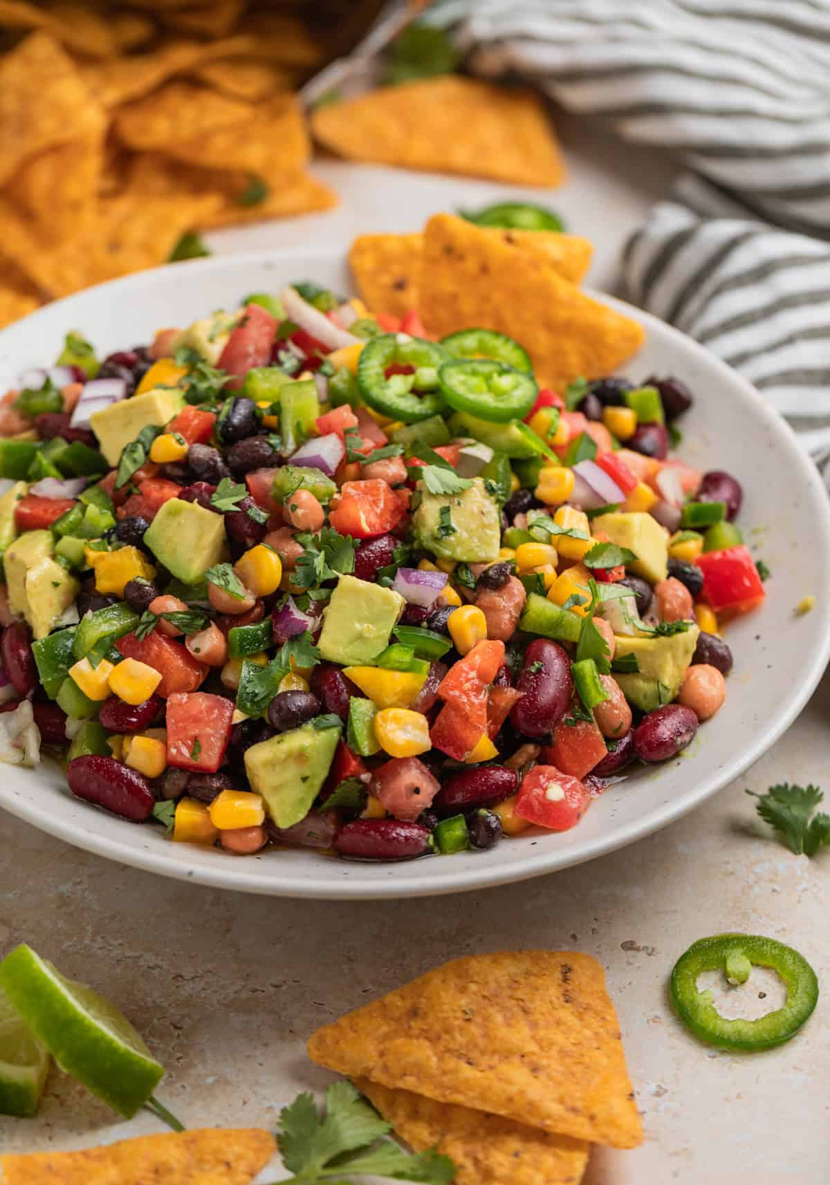 Chips dipped into bean and avocado salad with corn and topped with chopped cilantro.
