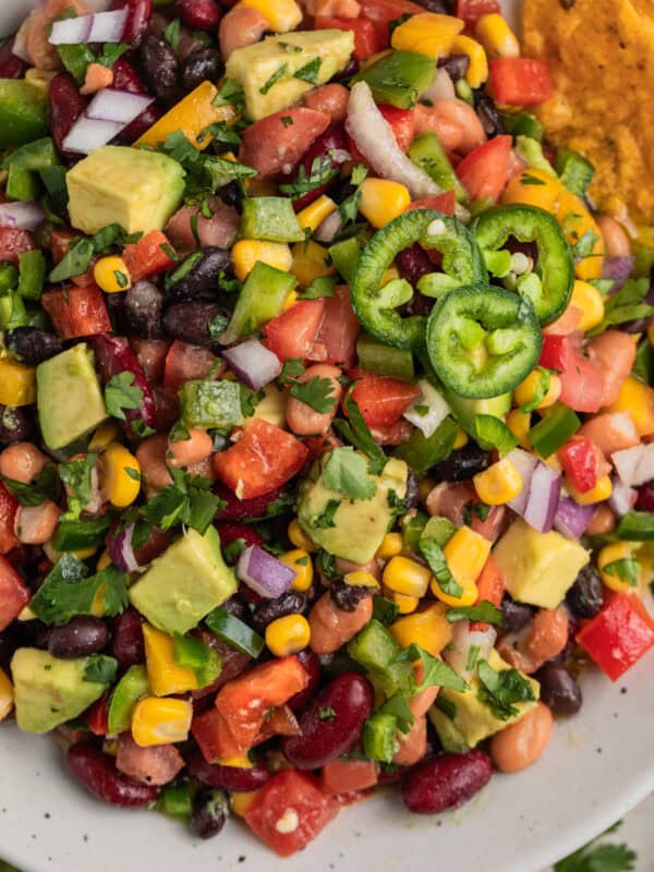 Tortilla chips dipping into bowl with kidney beans, black and pinto beans, vegetables, avocado, corn and more.