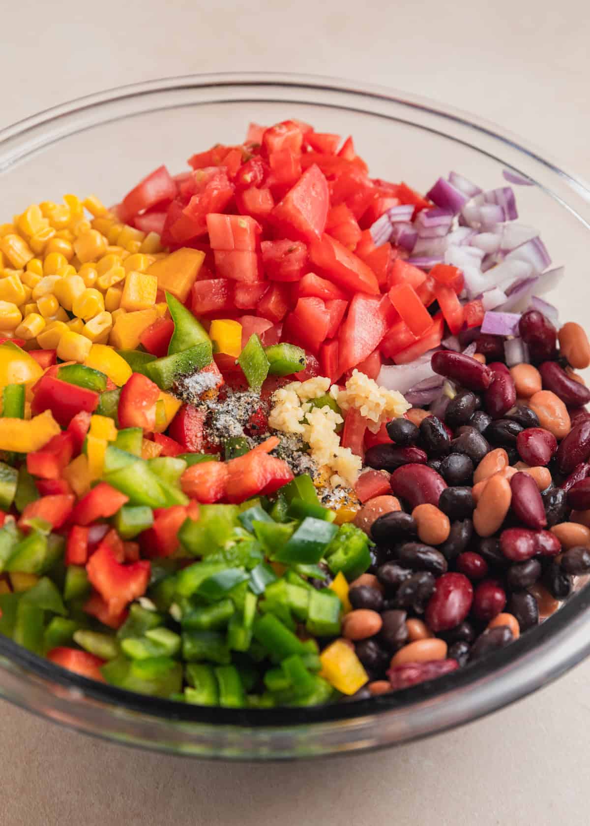 Diced tomatoes, pinto beans, black beans, kidney beans, chopped peppers and other ingredients in mixing bowl.