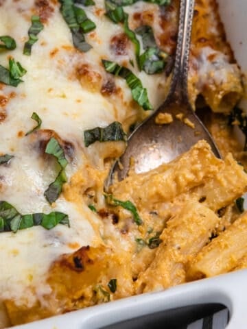 Spoon scooping out baked pumpkin rigatoni with fresh basil on top.