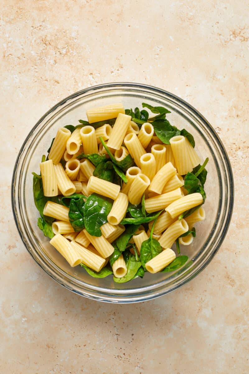 Rigatoni and spinach in glass mixing bowl.