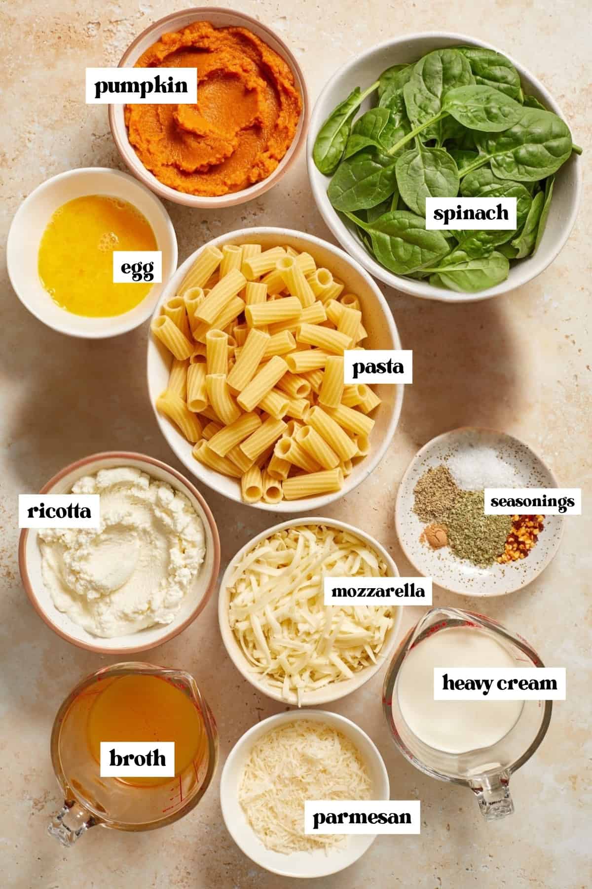 Spinach, noodles, broth, cream, pumpkin and other ingredients laying on surface prepped for recipe.