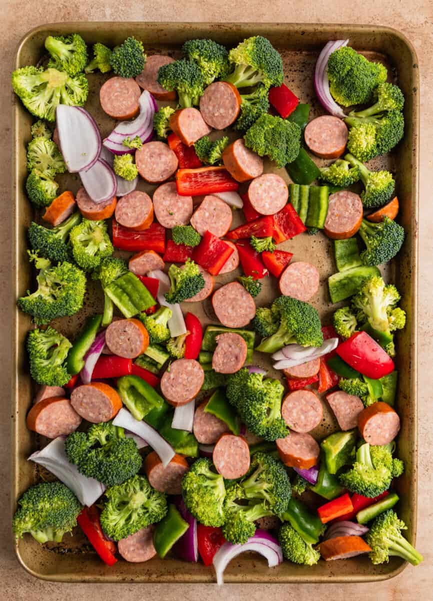 Kielbasa sausage sliced, chopped peppers and broccoli and onions on sheet pan.