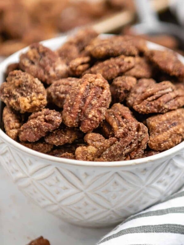 Bowl of candied pumpkin spiced pecans with striped linen and pan behind it.