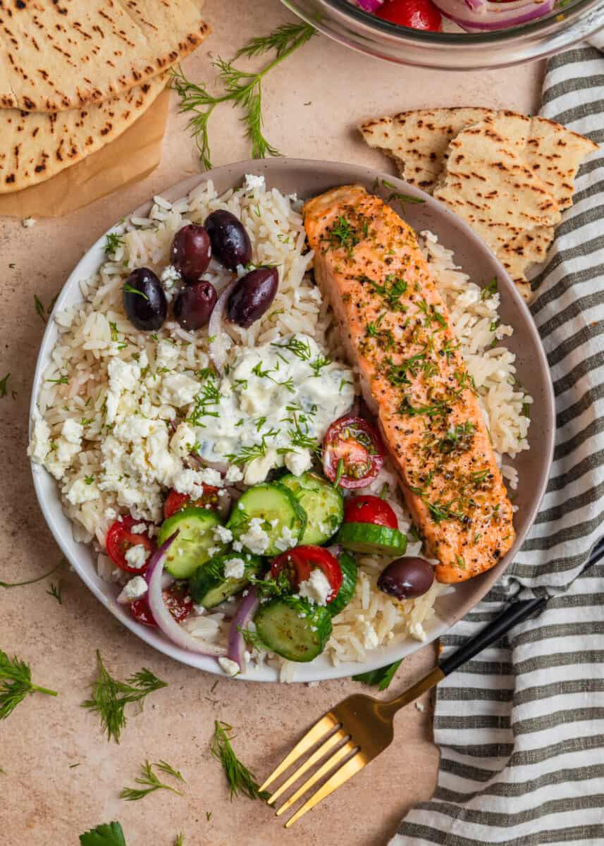Greek salmon bowl prepped and topped with cucumber salad and other ingredients.