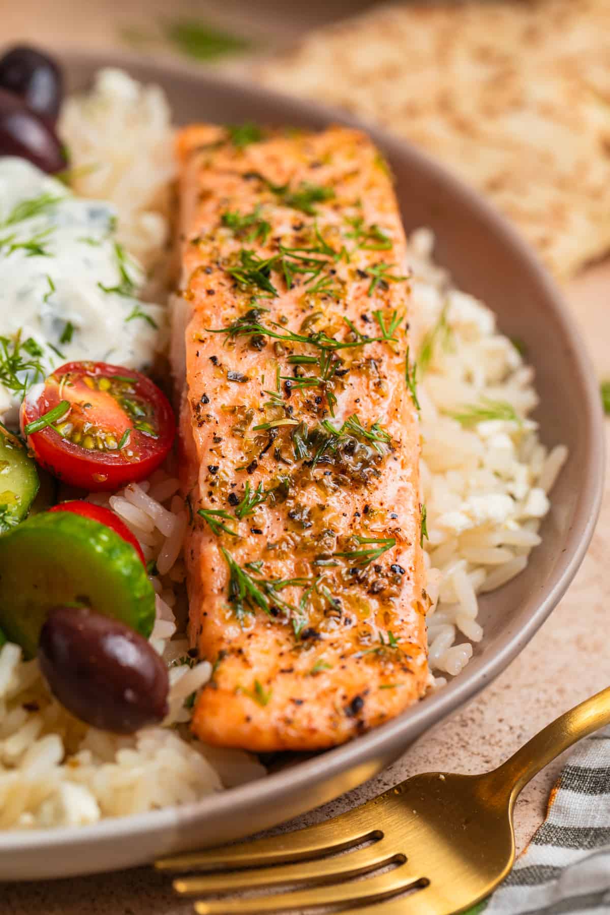 Greek salmon over a bed of rice with cucumbers, tomatoes, tzatziki sauce and other toppings.