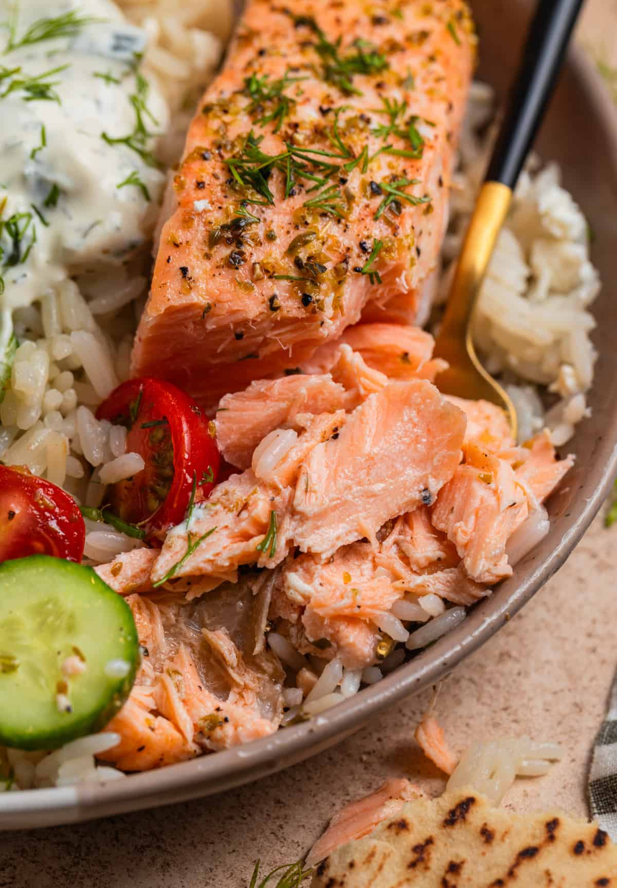 Salmon in dish with rice and veggies with fork and part of the salmon flaked.